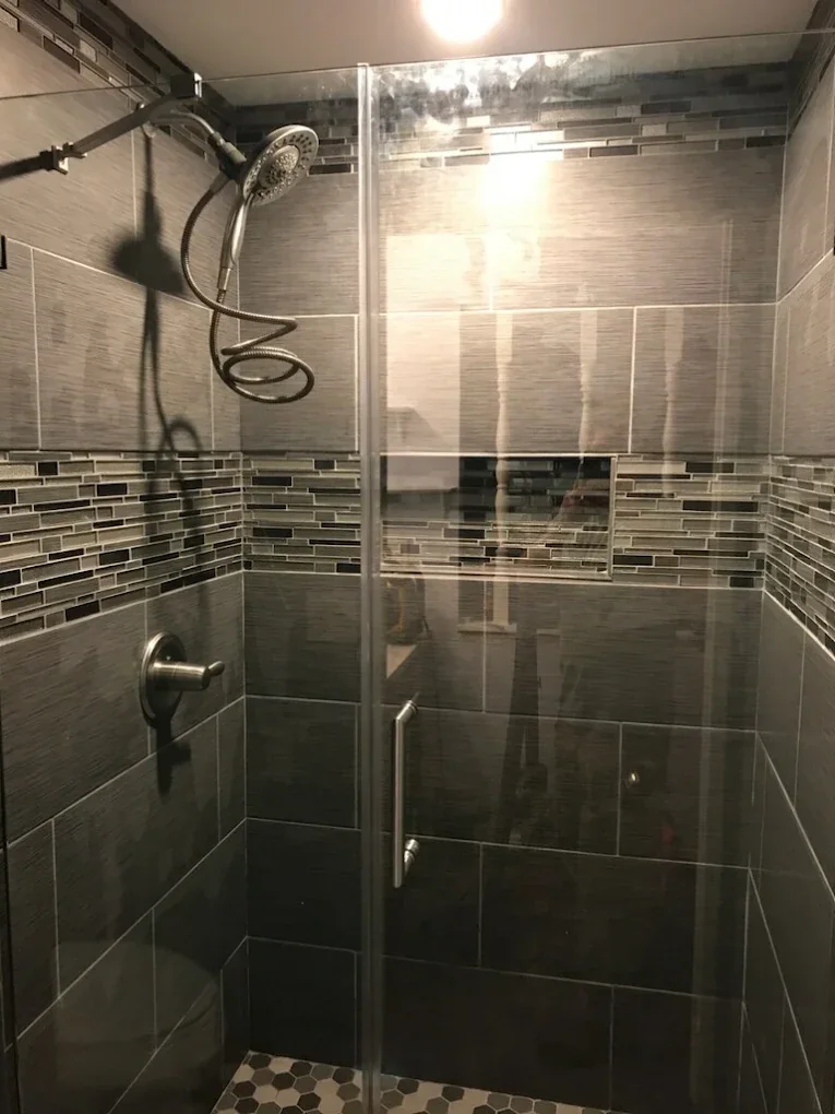 Glass-enclosed shower with dark gray tile and accent band