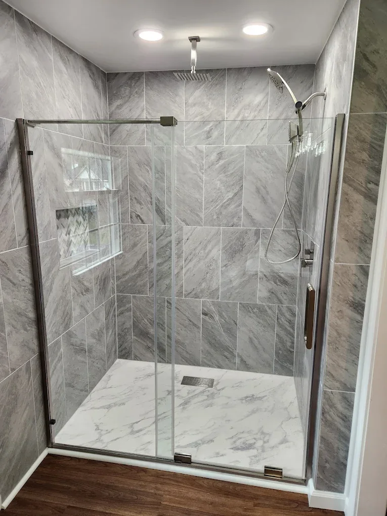 Glass walk-in shower with marble-look tile and recessed niche