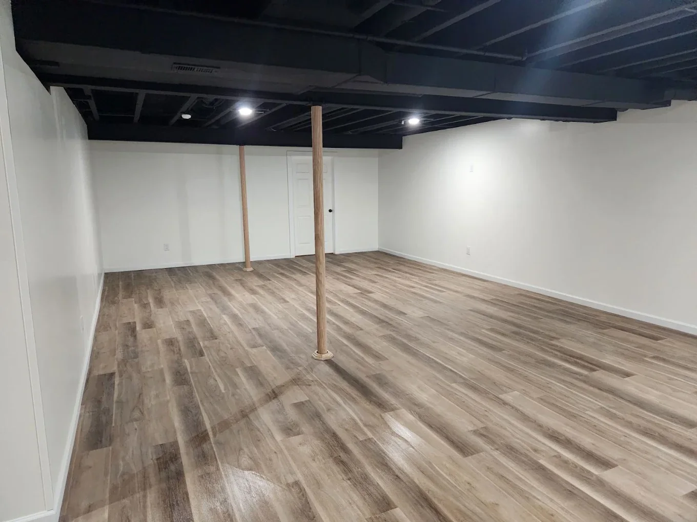 Open finished basement with wood-look floor and black ceiling